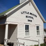 A white wooden building with a small bell tower, labeled Little Beaver School 1909 above two windows. A ramp with railing leads to the entrance under a small porch. The sky is clear and blue. Beach, SD