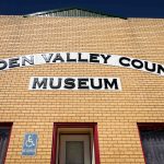 A yellow brick building with signs reading “Golden Valley County Museum” above the entrance and a blue reserved handicap parking sign near the doorway. Beach, SD