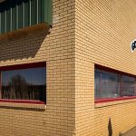 A tan brick building with red-trimmed windows, green roof edges, and a sign reading Golden Valley... above the entrance. The building sits on a sunny sidewalk under a clear blue sky. Beach, SD