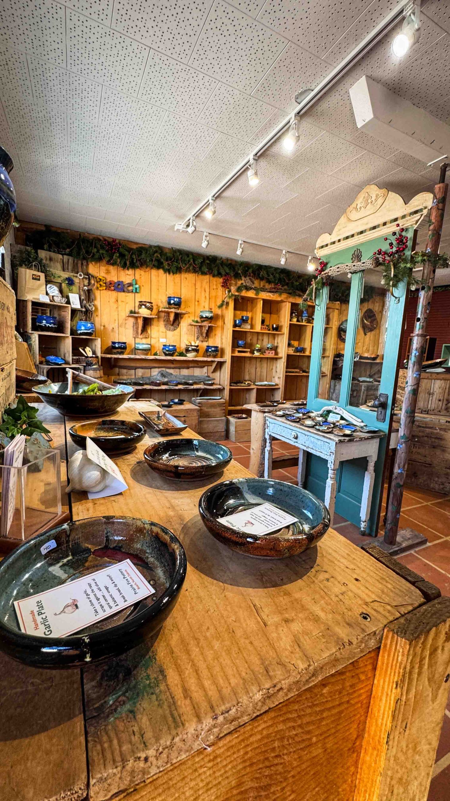 Handcrafted ceramic bowls displayed on a rustic wooden counter in a cozy Beach ND pottery shop, with shelves of pottery and decorative greenery lining the wooden walls in the background.
